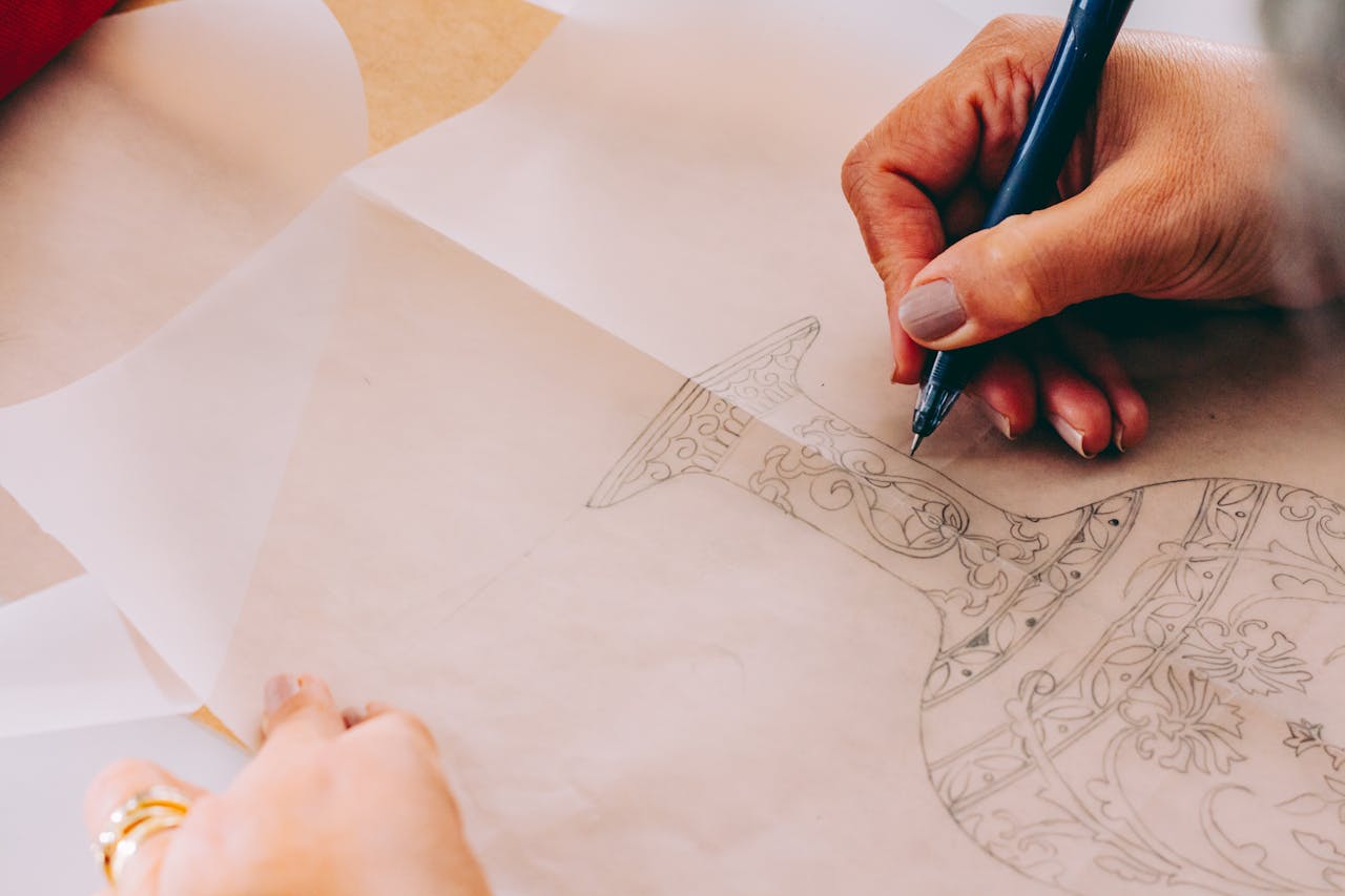 Artist drawing a detailed vase sketch on paper, focusing on intricate design patterns.